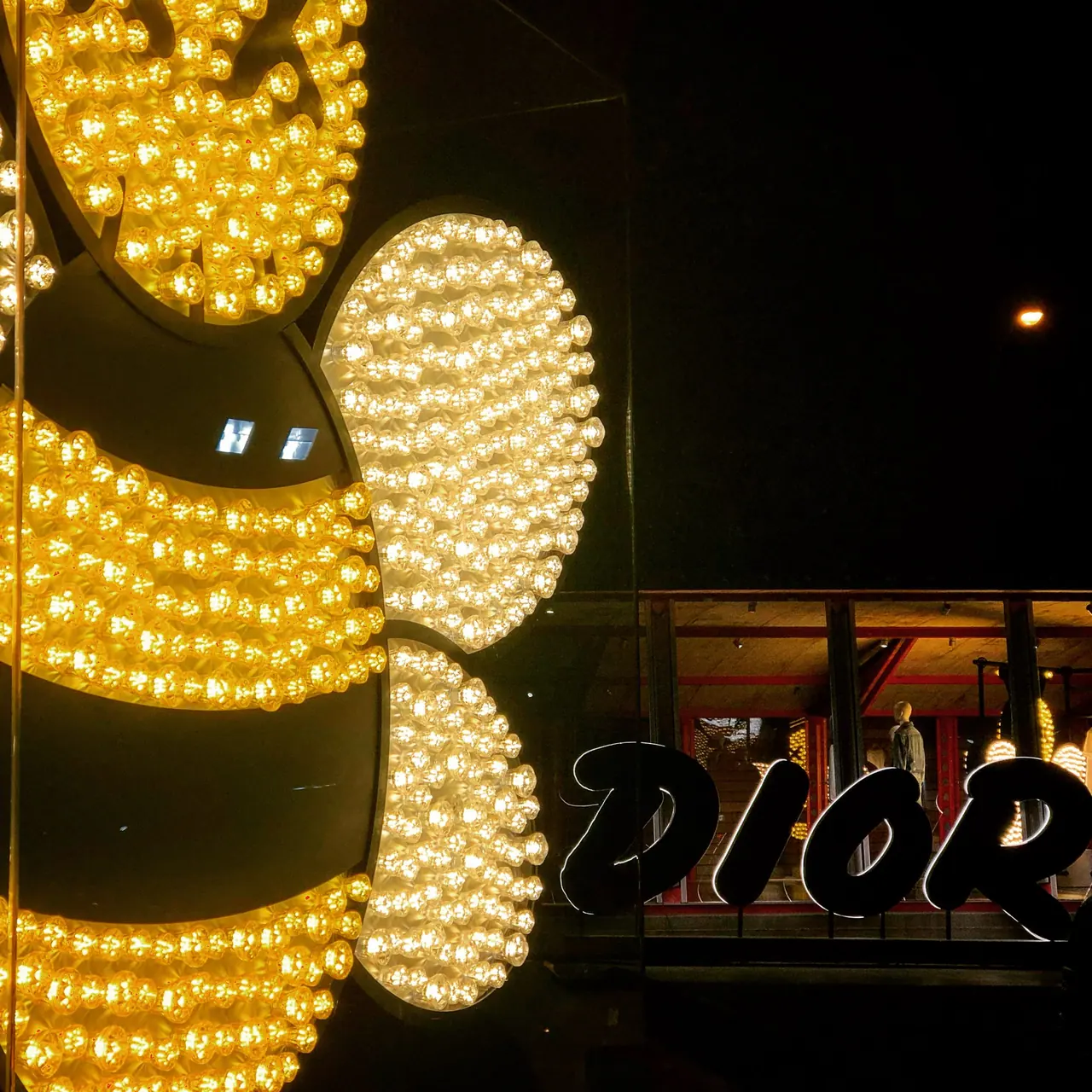 A bee-shaped display outlined in warm light bulbs at night.