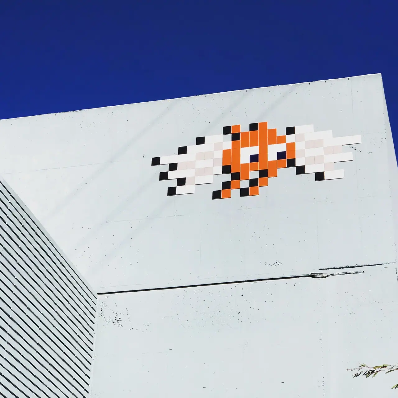 Pixel-style street art high on a white wall beneath a blue sky.