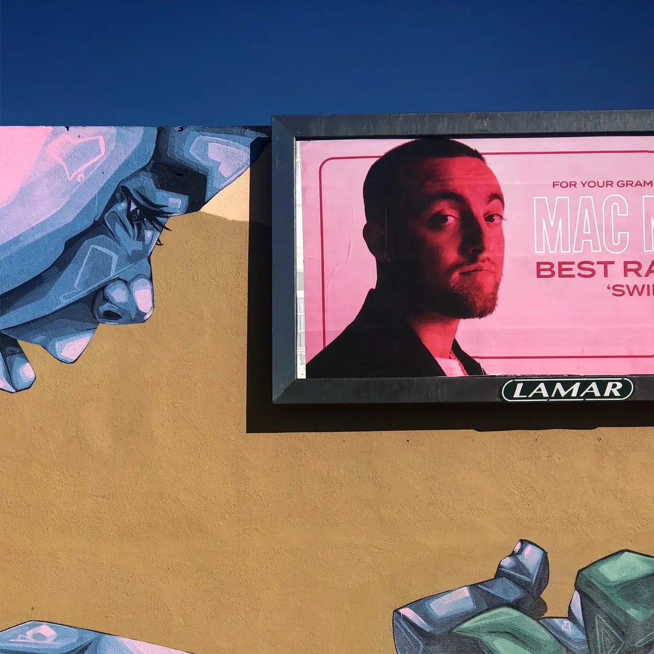 A pink billboard above a painted city wall.