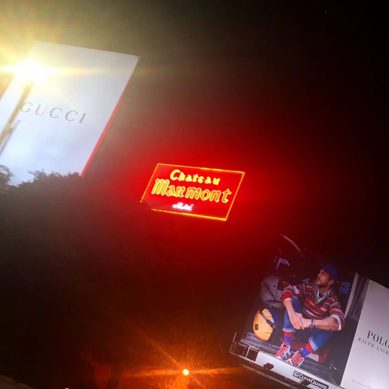 The red Chateau Marmont neon sign between illuminated billboards at night.