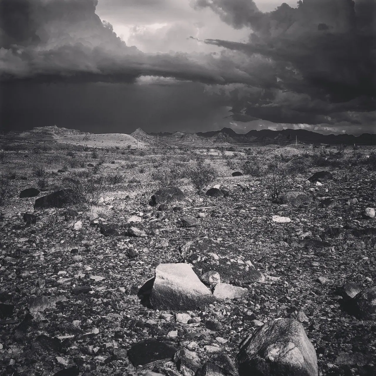 Dark monsoon clouds over a rocky desert landscape.