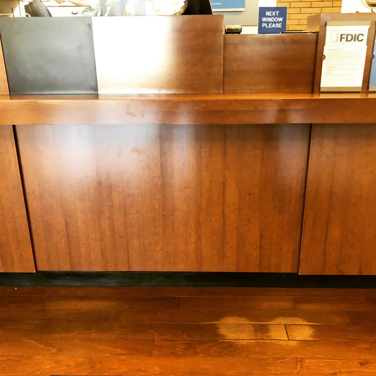 A wooden bank counter above a patch of worn flooring.