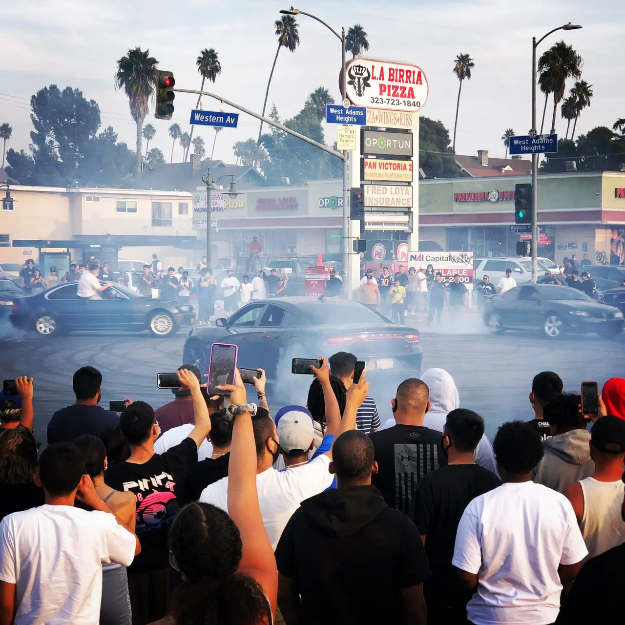 Spectators and tire smoke at a crowded street intersection.
