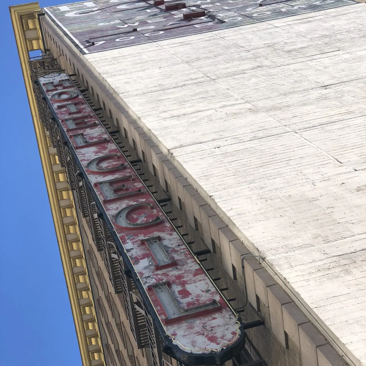 A weathered vertical hotel sign viewed from below.