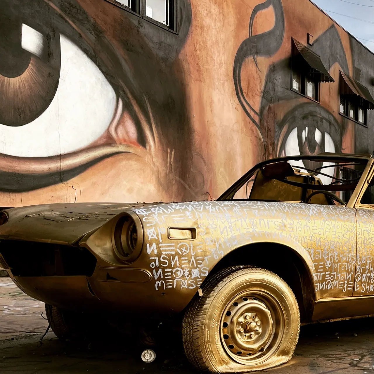 A weathered car beneath a large painted eye.