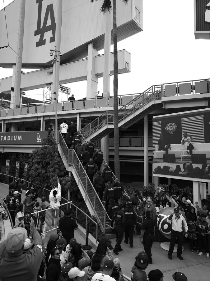A crowd and security staff gathered beneath a stadium staircase.