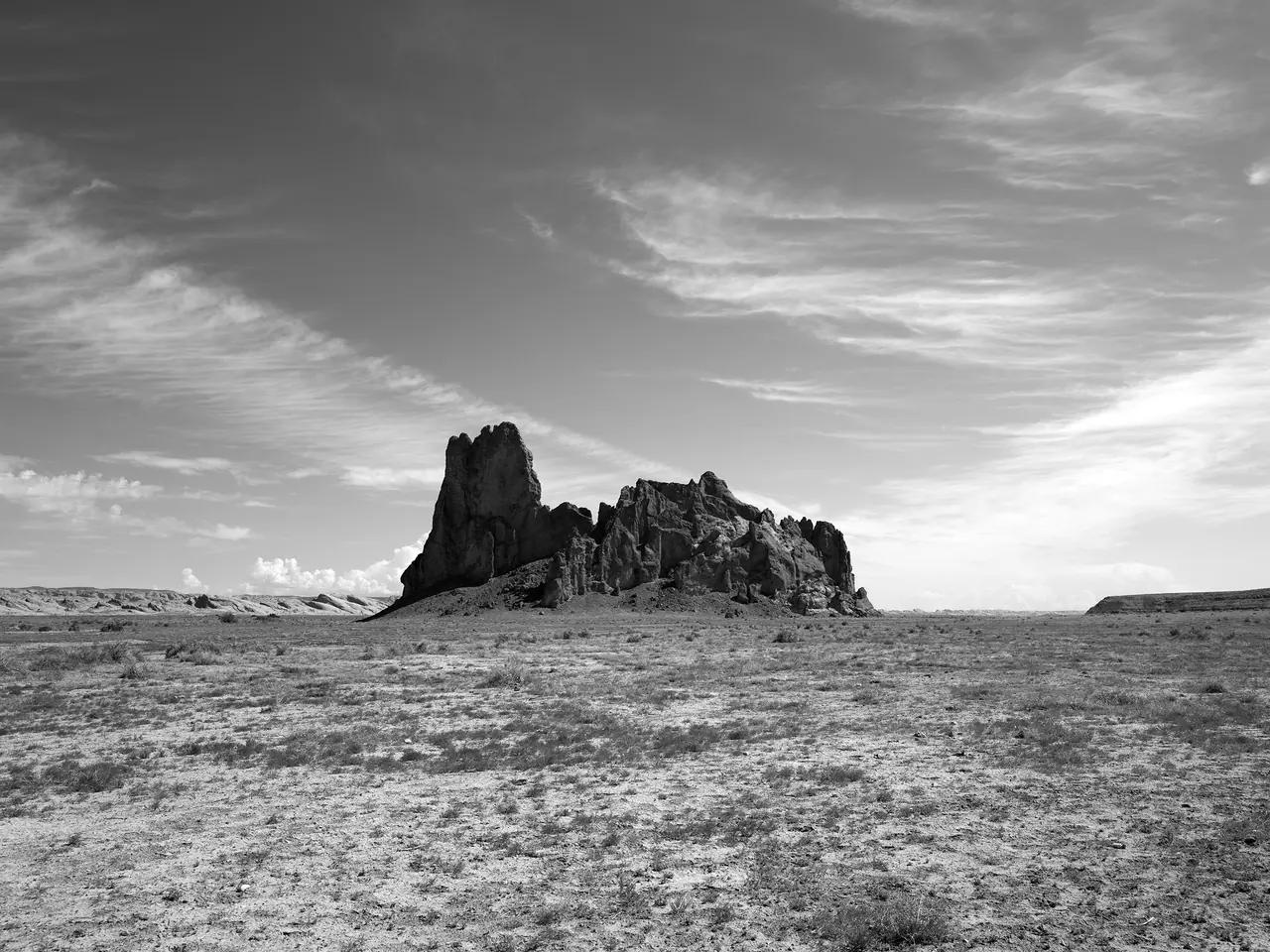 An isolated rock formation beneath sweeping clouds on a desert plain.