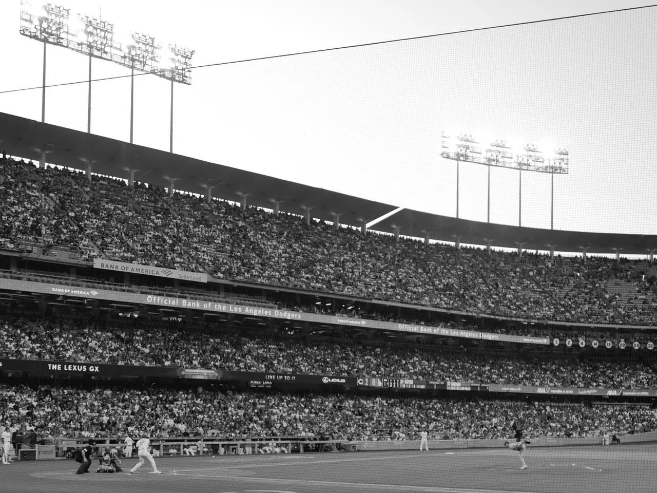 A baseball game beneath stadium lights and a bright afternoon sky.