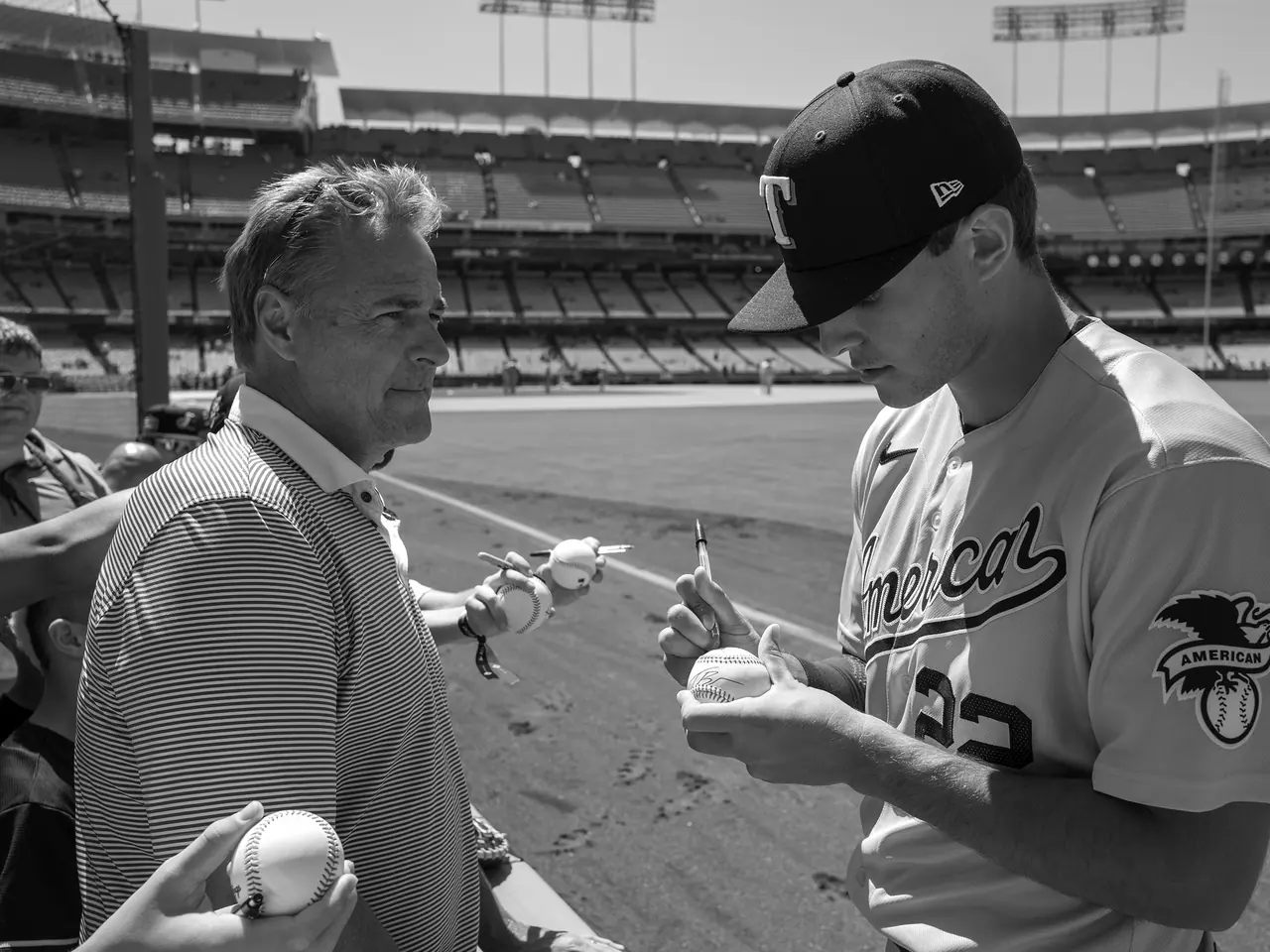 A baseball player signing an autograph beside a fan.