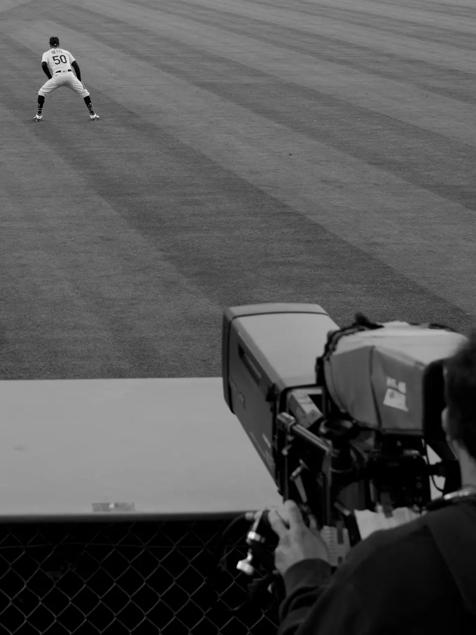 A broadcast camera watching an outfielder from beside the field.