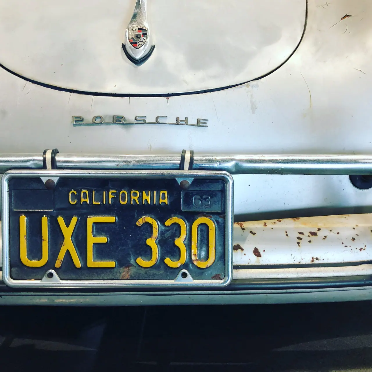 The weathered rear of a vintage Porsche with a blue California license plate.