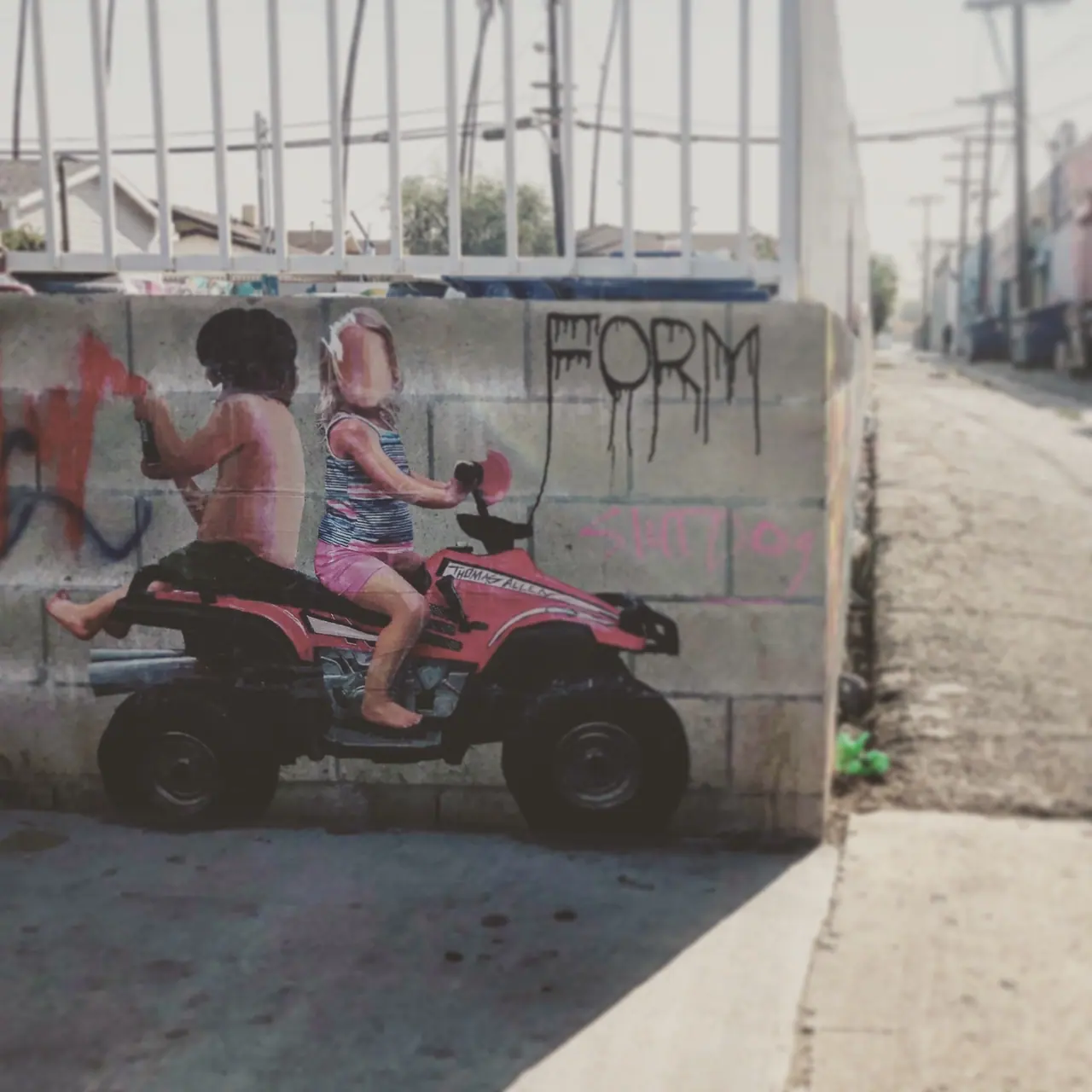 An alley mural depicting children on a red all-terrain vehicle.