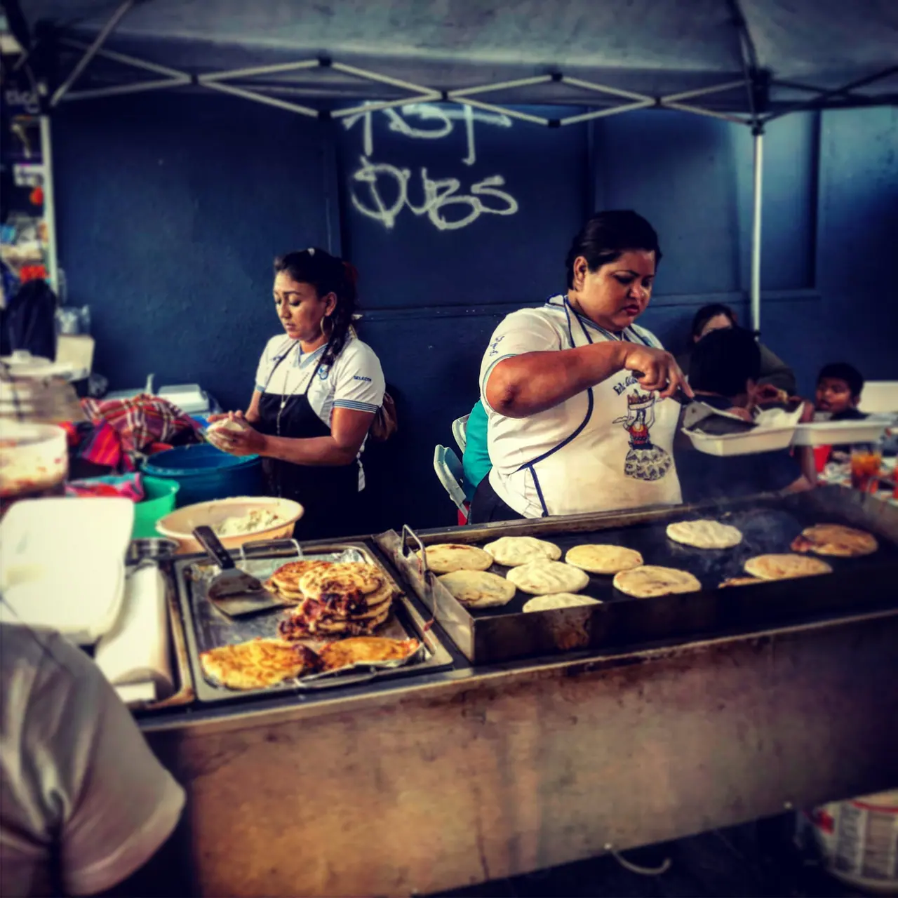 Pupusas cooking at a sidewalk food stall.