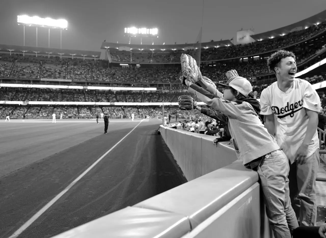 A young fan reaching over a stadium railing with a baseball glove.