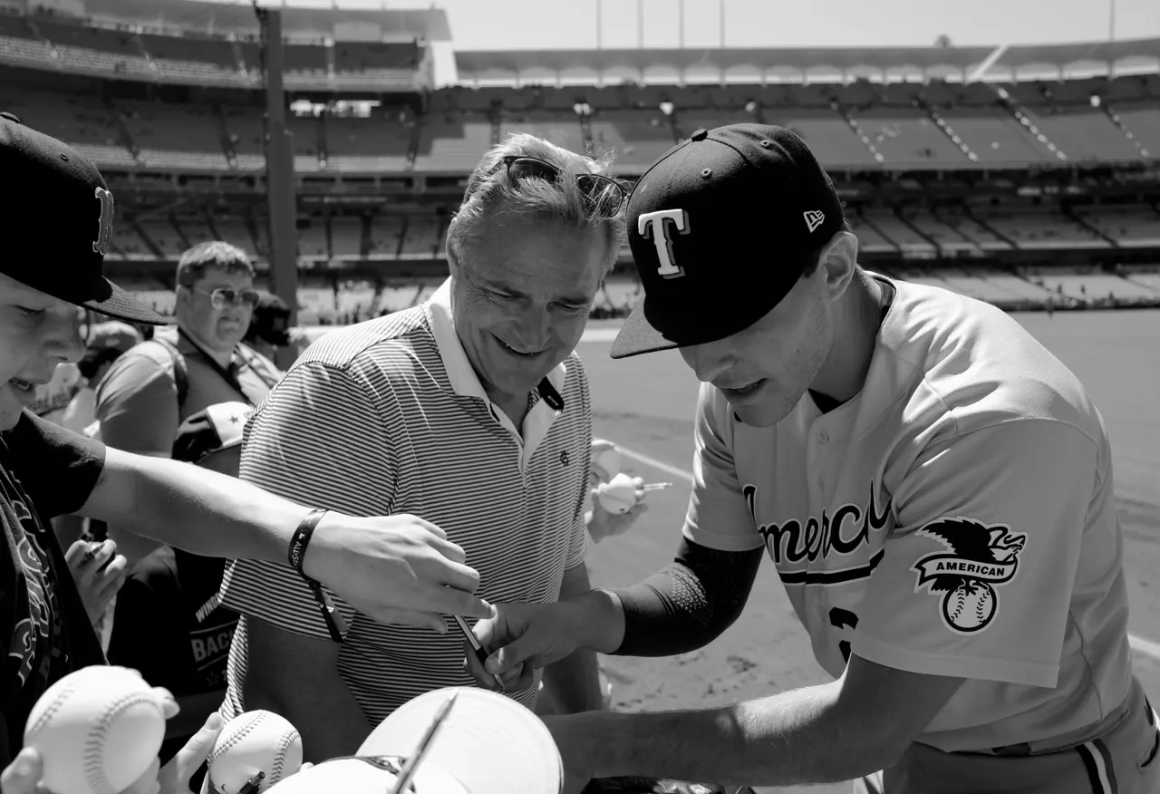 A fan smiling while a baseball player signs a baseball.