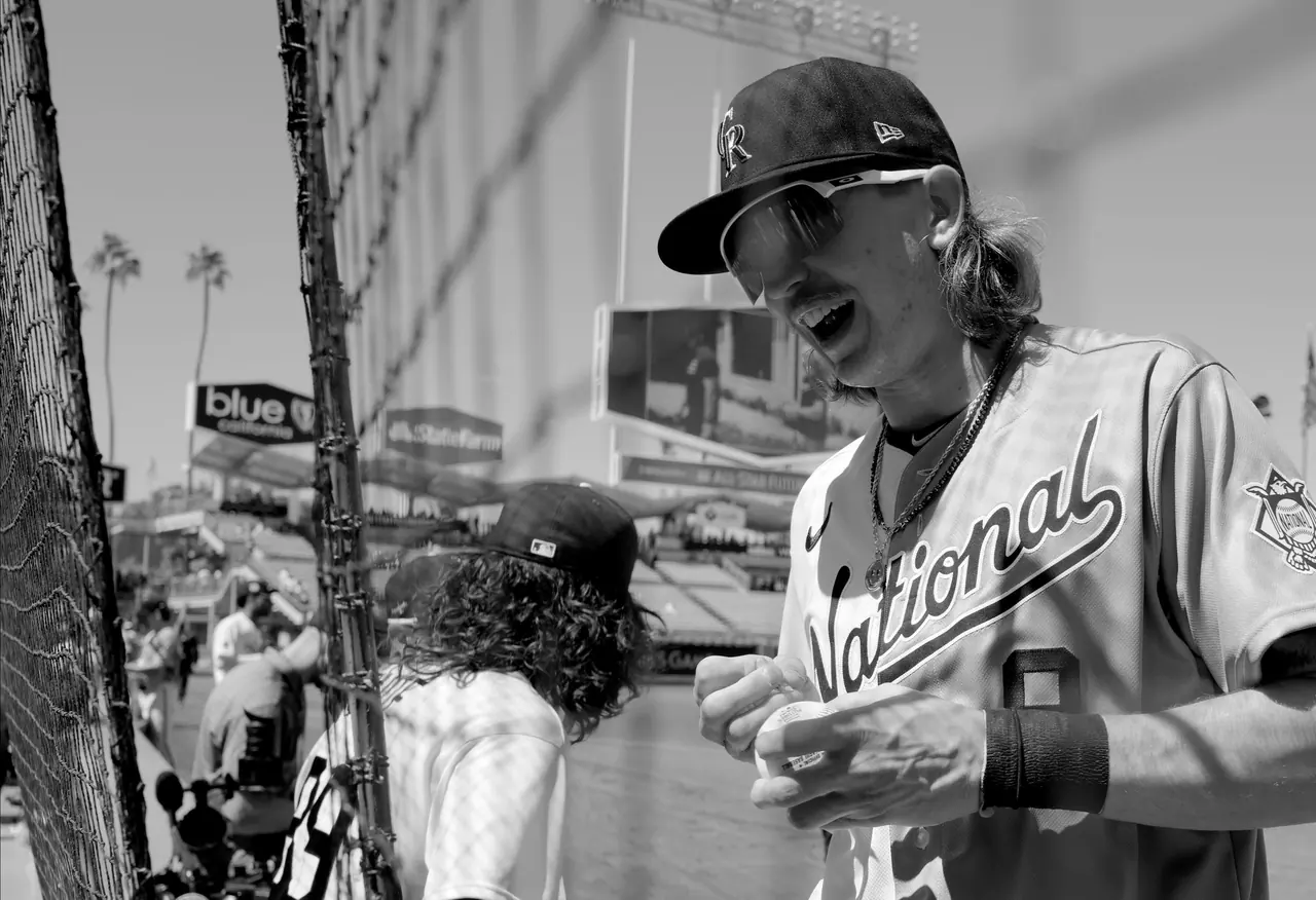 A smiling baseball player wearing sunglasses near the stadium fence.