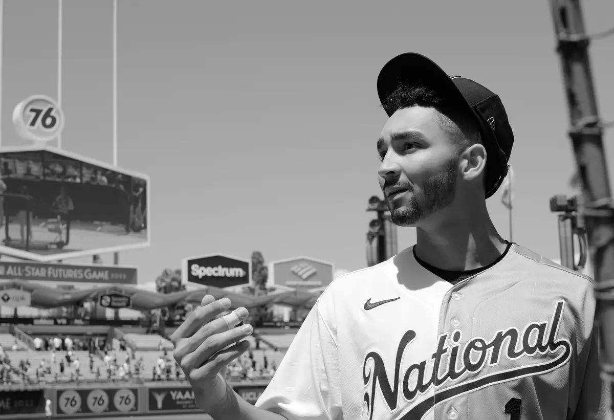 A baseball prospect standing beside the field beneath a clear sky.