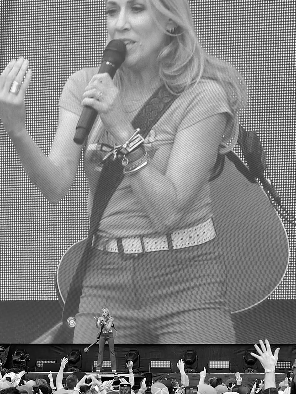 A singer onstage beneath a giant live video screen and raised audience hands.
