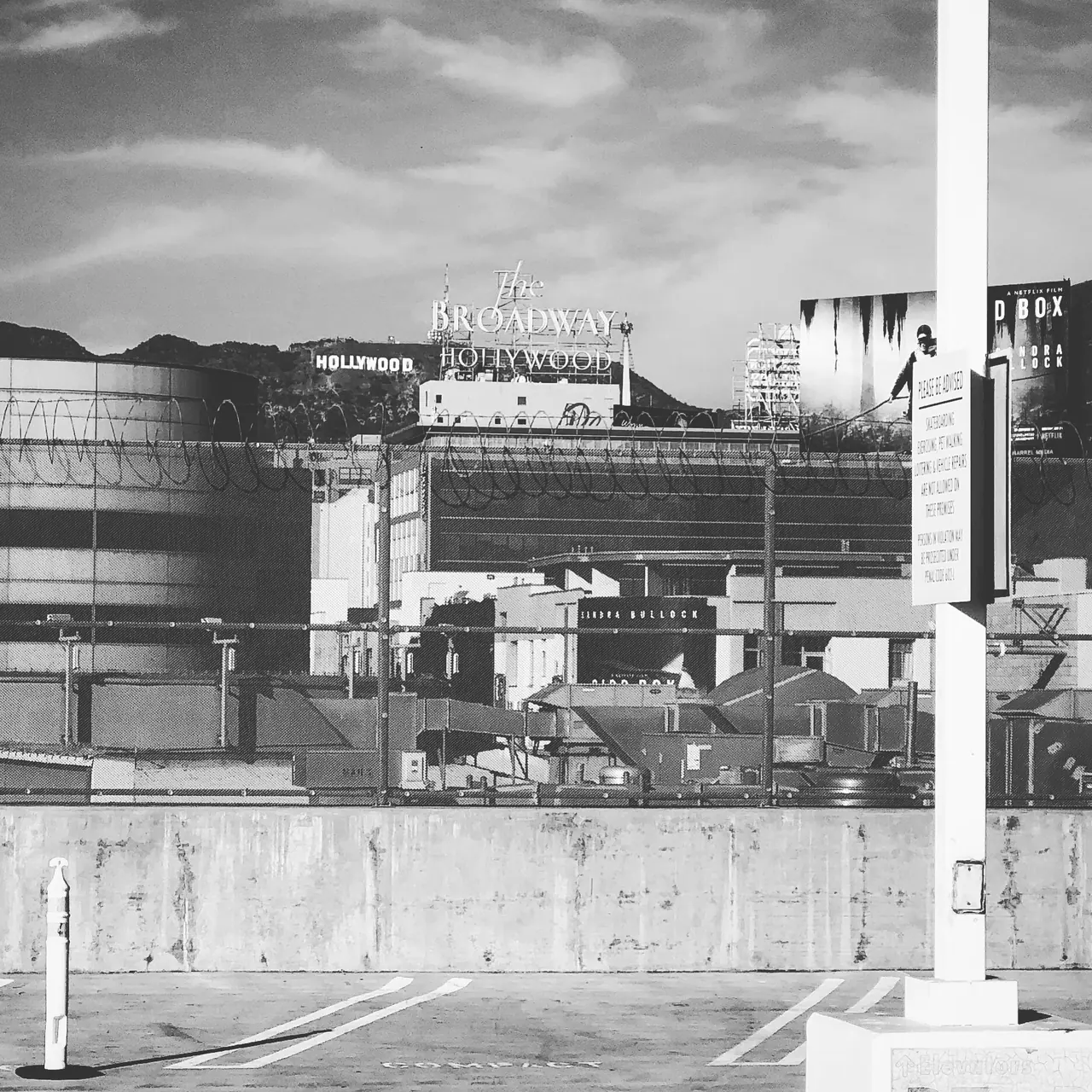 The Hollywood sign above rooftops and a parking deck, in black and white.