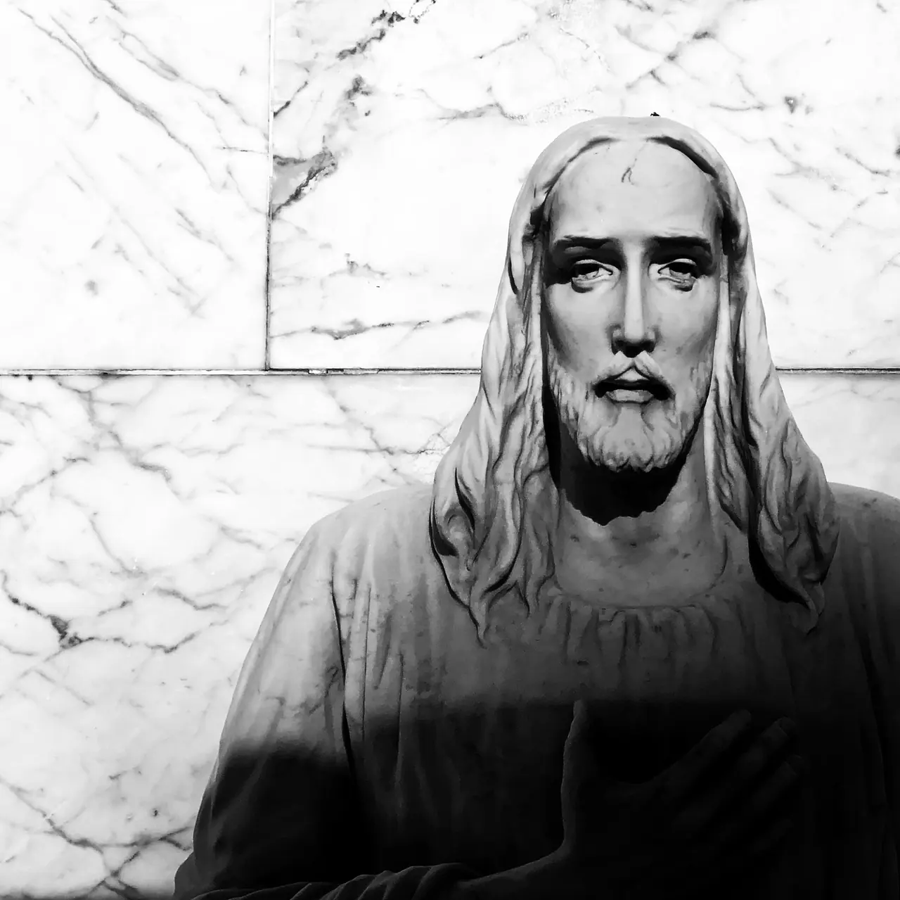 Light and shadow across a religious statue against a marble wall.